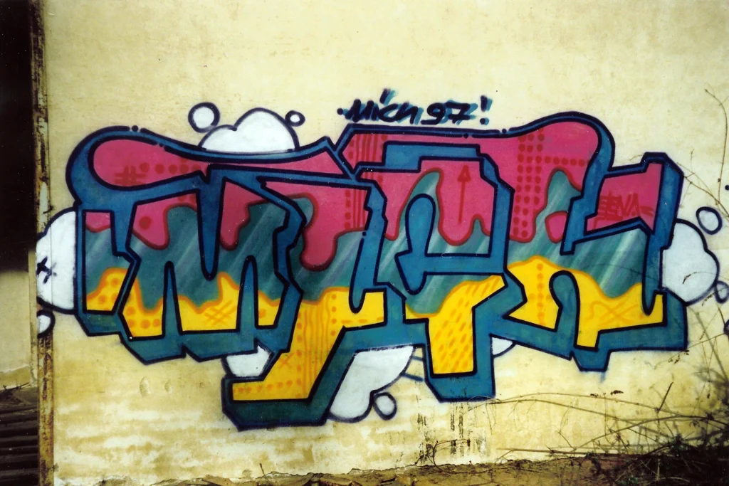 Murales su muro di cemento con lettering esteso blu e arancio, Cairate 1997.