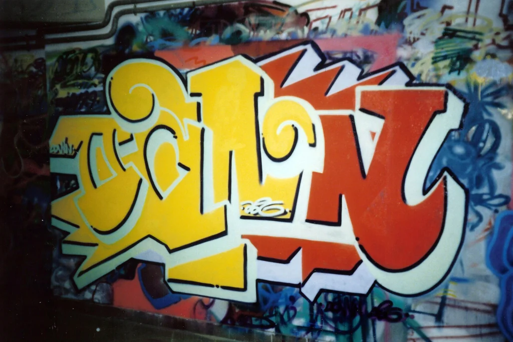 Murales rosso e grigio su parete metallica, lettering bold e dettagli pink, Tradate 1997.