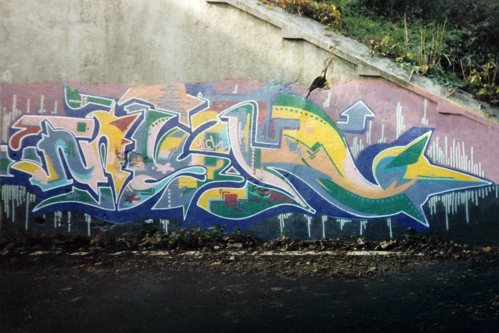 Graffiti colorato su muro inclinato con forme fluide e toni pastello, Tradate 1997.