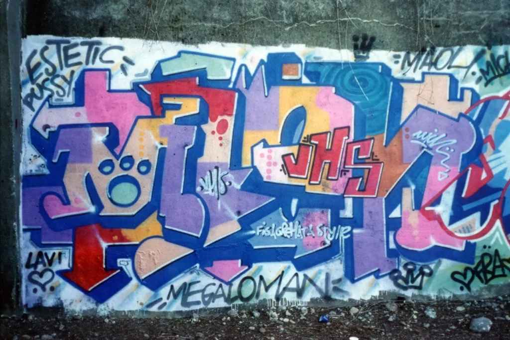 Murales colorato con lettering viola e arancione su muro grigio, Venegono 1997.