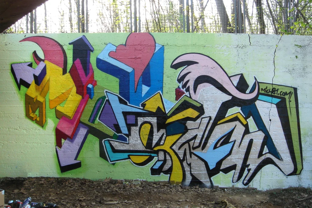 Graffiti 3D colorato con frecce e forme astratte su muro verde, Tradate 2005.