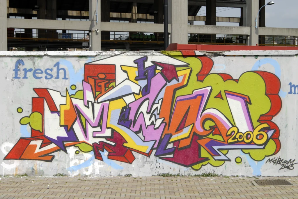 Graffiti colorato con lettering tridimensionale su pannello bianco, realizzato ad Arona nel 2006.