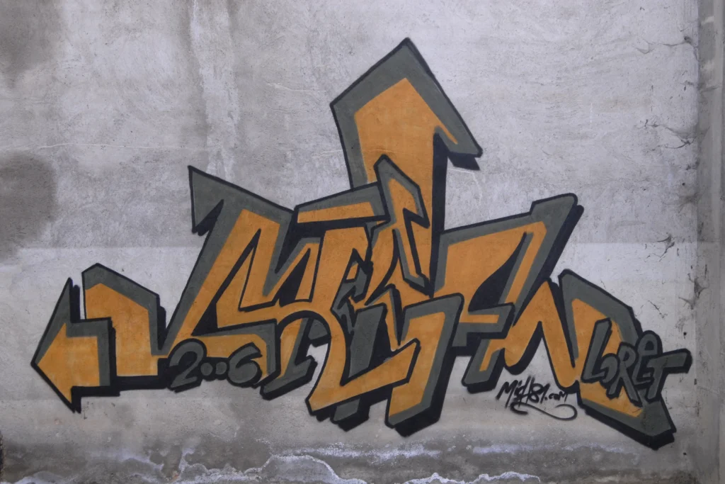 Graffiti tridimensionale arancio e con contorno nero su muro grezzo, firmato Mich81, Cairate 2006.