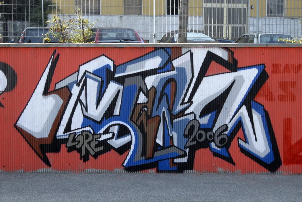 Graffiti in blu, bianco e marrone su muro rosso, Milano 2006.
