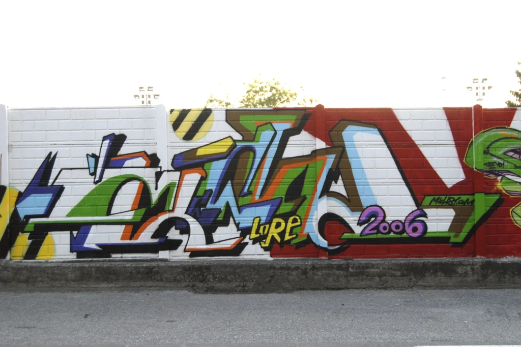 Murale con graffiti geometrici e colori vivaci su muro bianco, Somma Lombardo 2006.