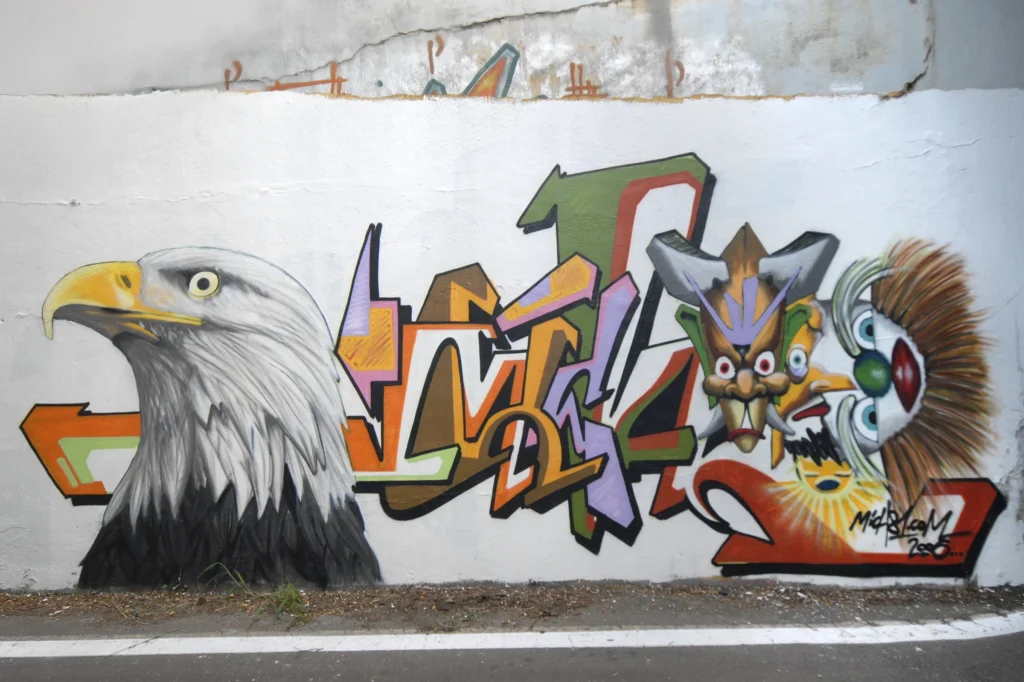 Murale con aquila realistica, maschere colorate e lettering geometrico, Tradate 2006.