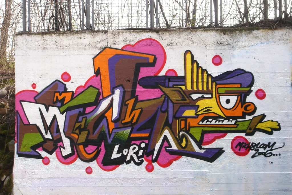 Graffiti colorato con lettering e personaggio stilizzato su muro bianco, Tradate 2006.