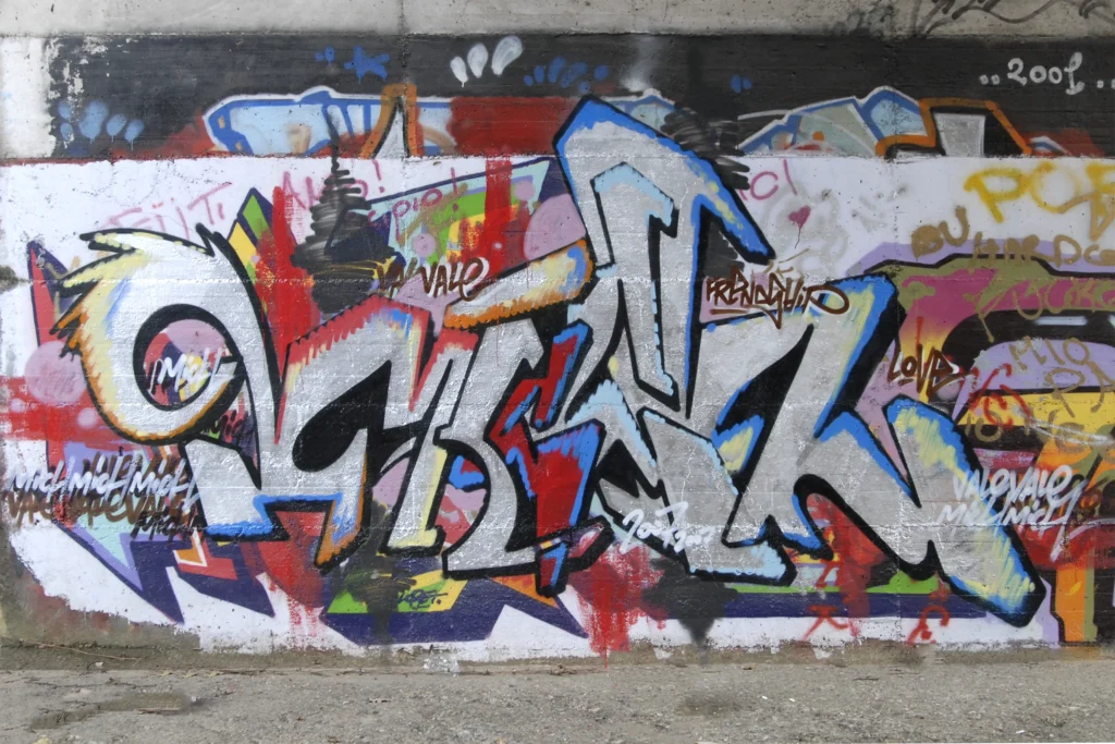 Graffiti con lettering argentato e contorni blu su fondo multicolore, Tradate 2007.